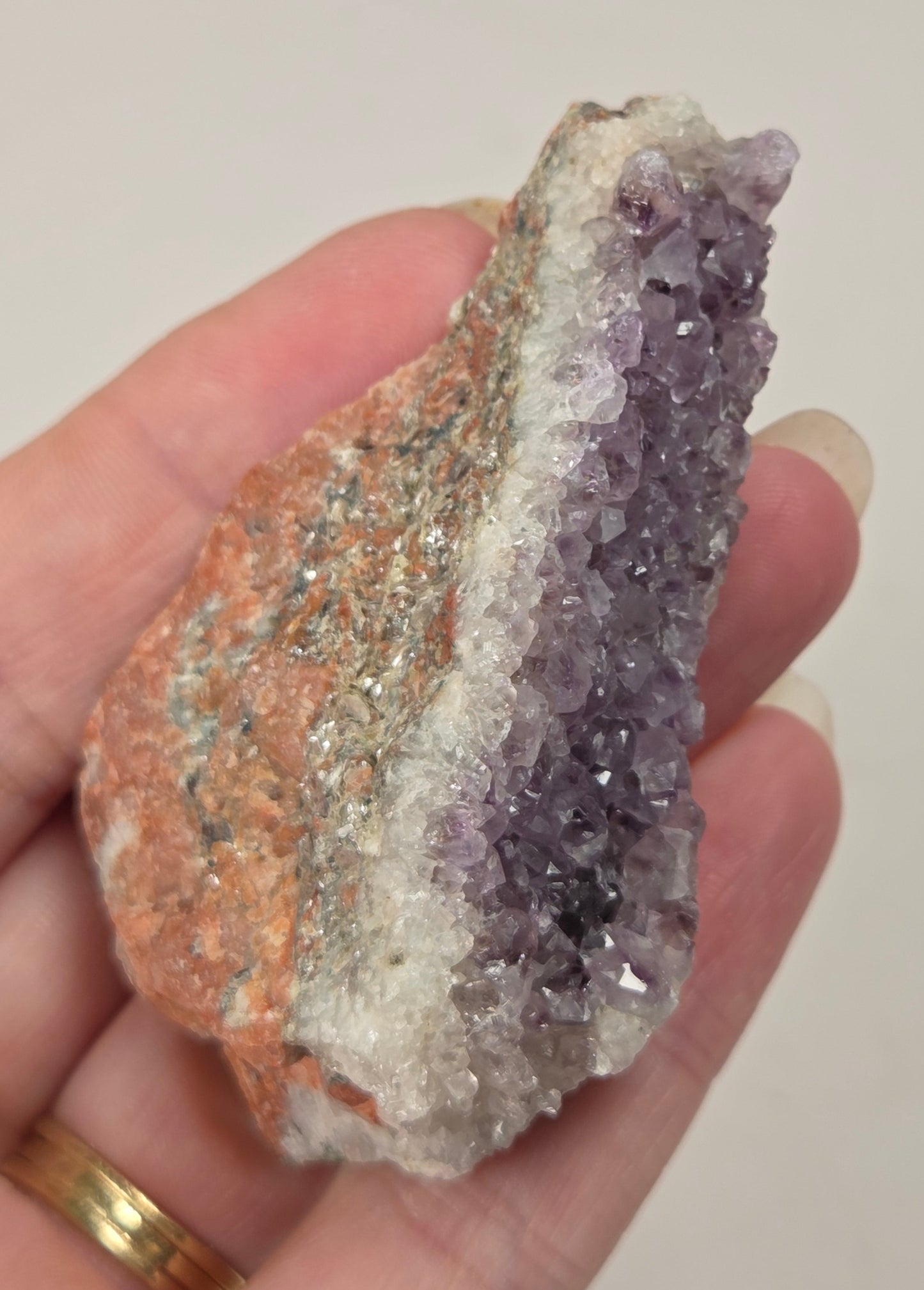 A hand holding a raw crystal cluster specimen showing a dual-tone amethyst and copper geode formation.
