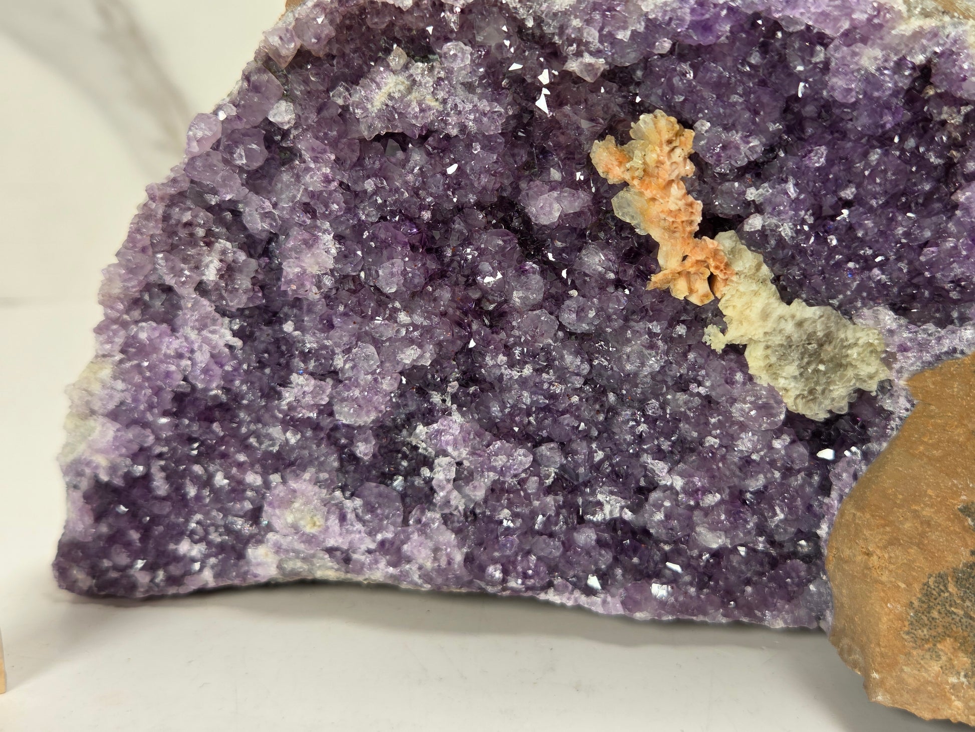 Close-up of a raw amethyst geode specimen with a purple crystal cavity and brown matrix, displayed on a white surface 