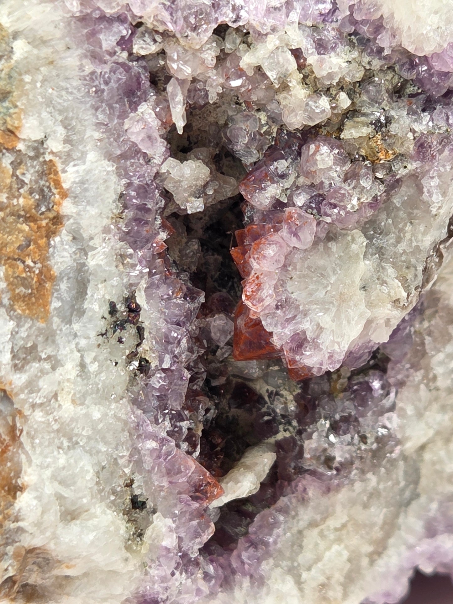 Close-up of a mineral specimen with predominantly lavender-purple crystal clusters, mixed white and translucent quartz-like areas, and a small reddish-brown inclusion near the center.