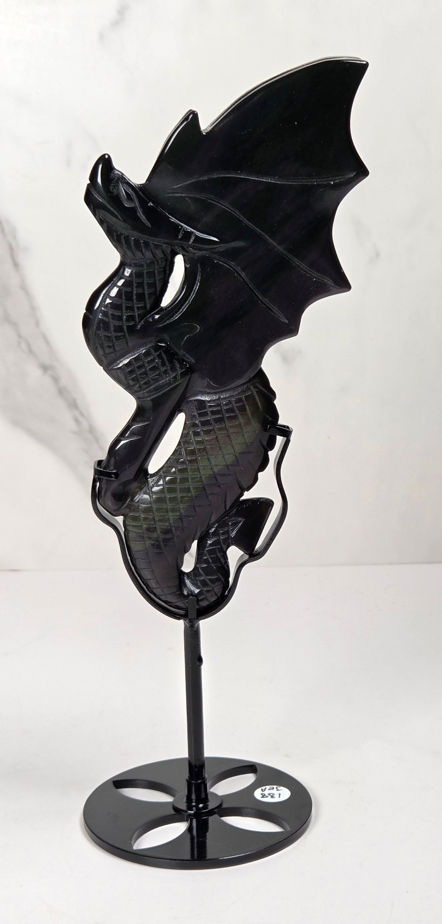 A black dragon figurine with detailed scales and wings, mounted on a black metal stand with a circular base, set against a white marble-patterned background.