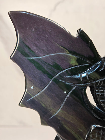 A close-up of a glossy dark carved object, likely a decorative sculpture or tray, showing a bat-like wing shape with carved line details and a textured lower section, photographed against a light neutral background.