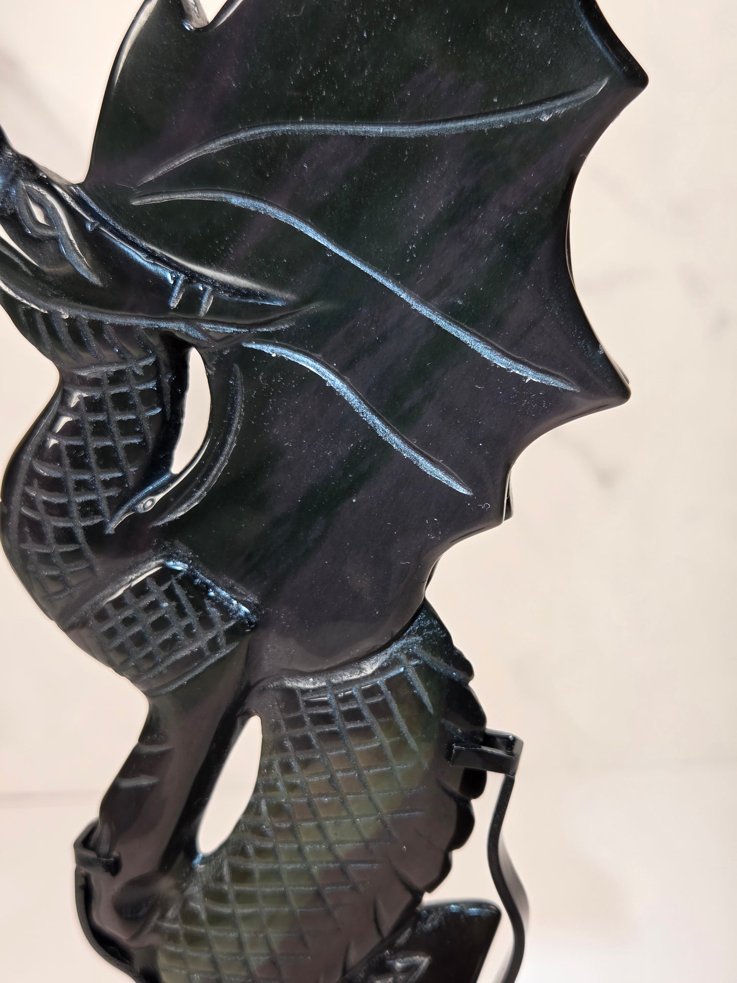 A close-up of a glossy black carved dragon figurine, showing detailed scales and wing textures against a light beige background.