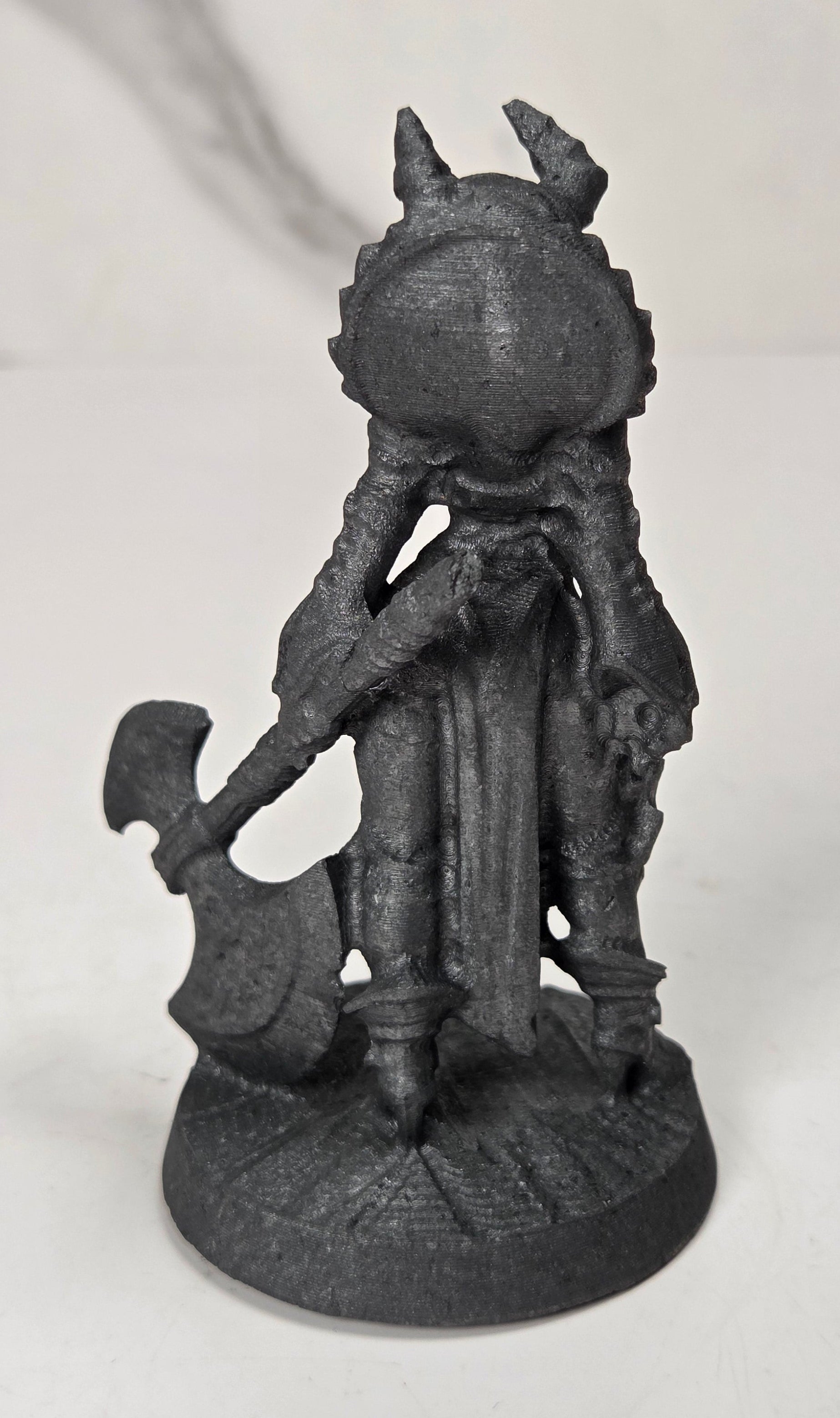 A small dark gray fantasy figurine of a horned character holding an axe, standing on a round base against a light gray background.