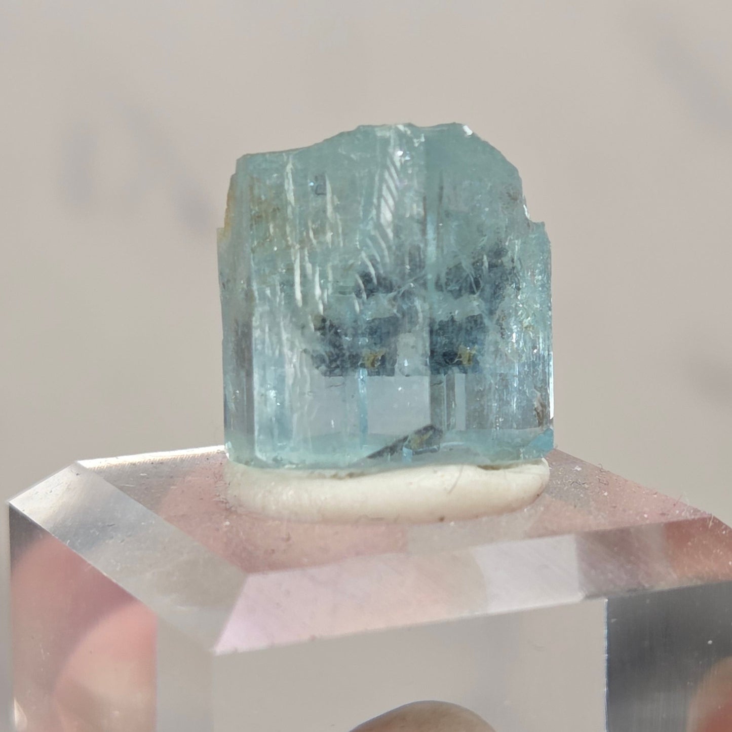 A hand holding a small clear acrylic block containing a pink heart-shaped piece, with a faceted light blue gemstone or crystal mounted on top.