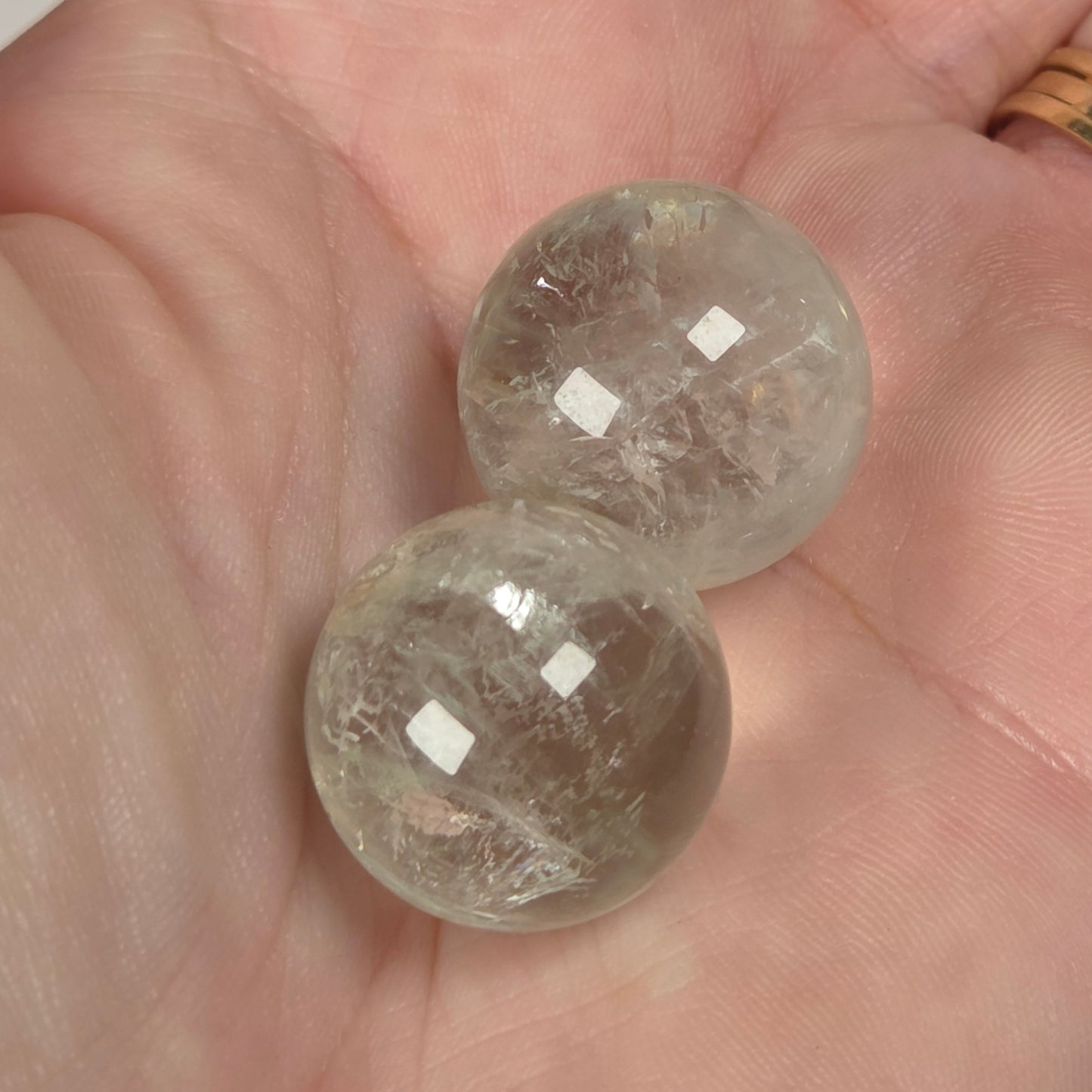 Two clear, faceted glass or crystal spheres resting on an open hand, with a gold ring visible on the person's finger.