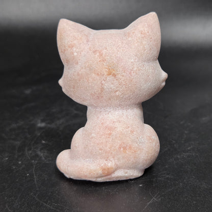 A small pink cat figurine shown from the back, made of a textured stone-like material, set against a dark gray background.