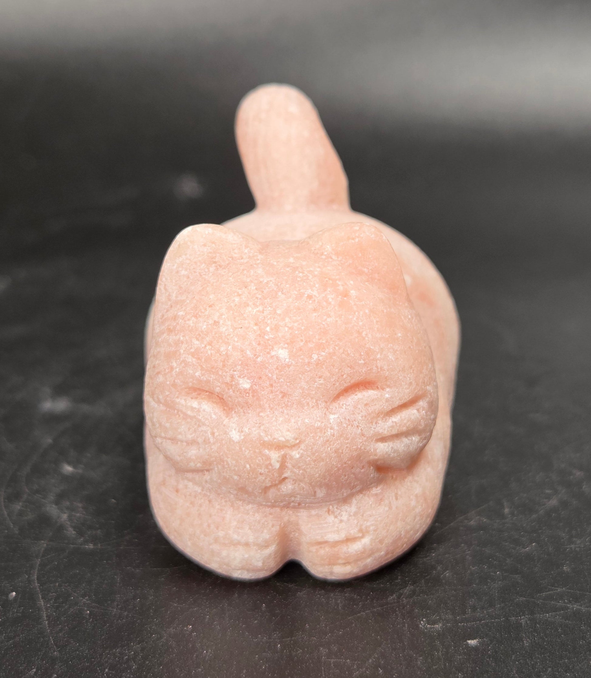 A small pink cat figurine with closed eyes, standing on a dark gray surface.