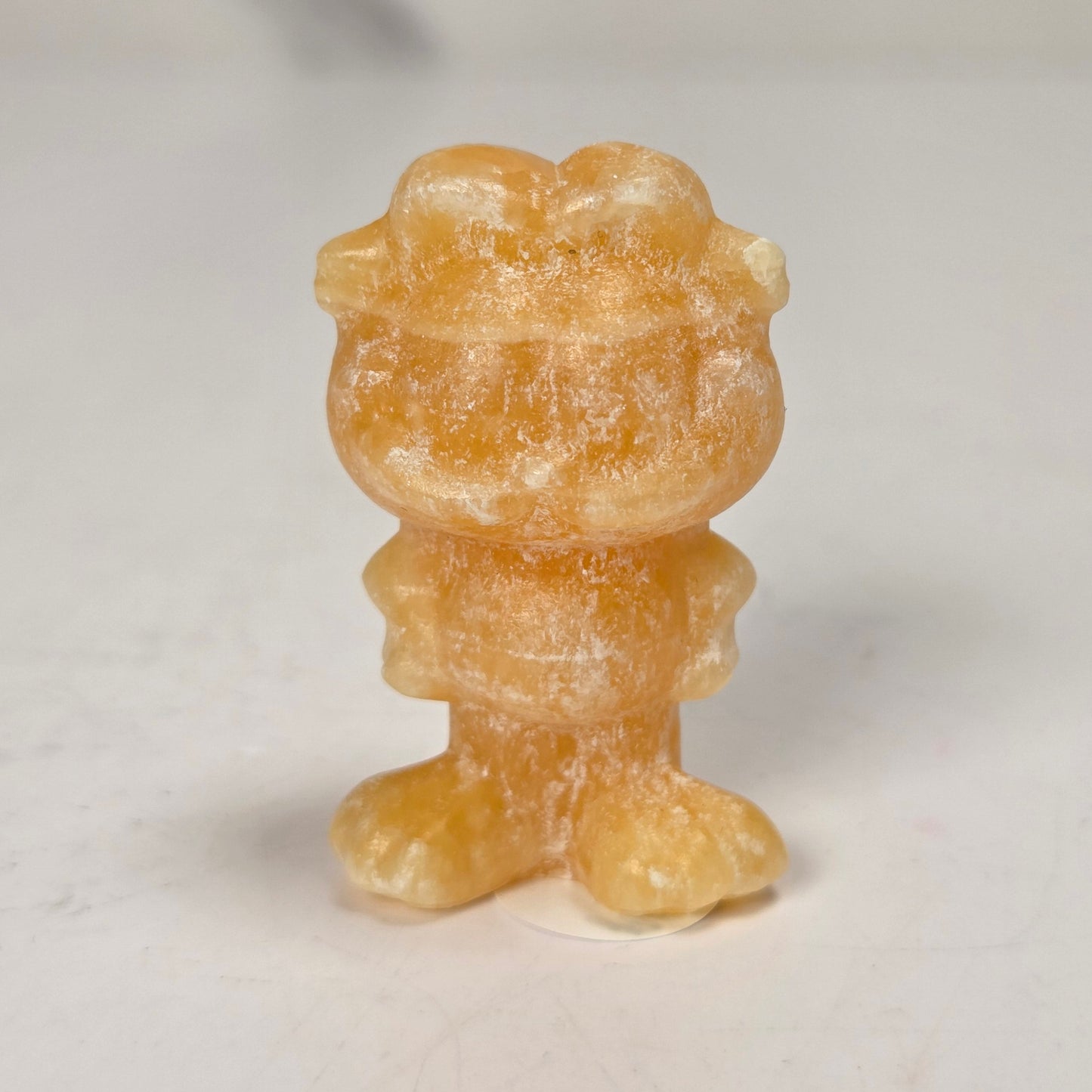 A small, translucent amber-orange carved figurine of a cartoon character, standing on a light gray surface with a blurred gray background.