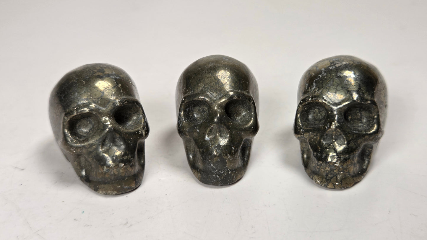Three small metallic skull-shaped objects arranged side by side on a plain light background.