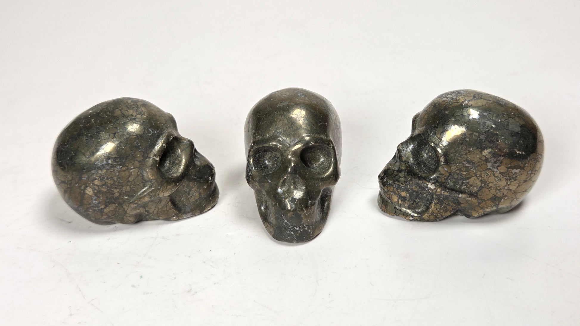 Three small polished skull figurines in a dark metallic finish, arranged side by side on a plain white surface.