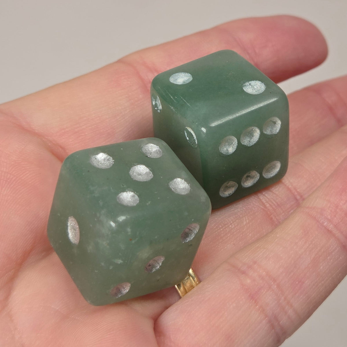 Two translucent green dice-shaped jewelry pieces resting on an open hand, with a white marble-patterned background.