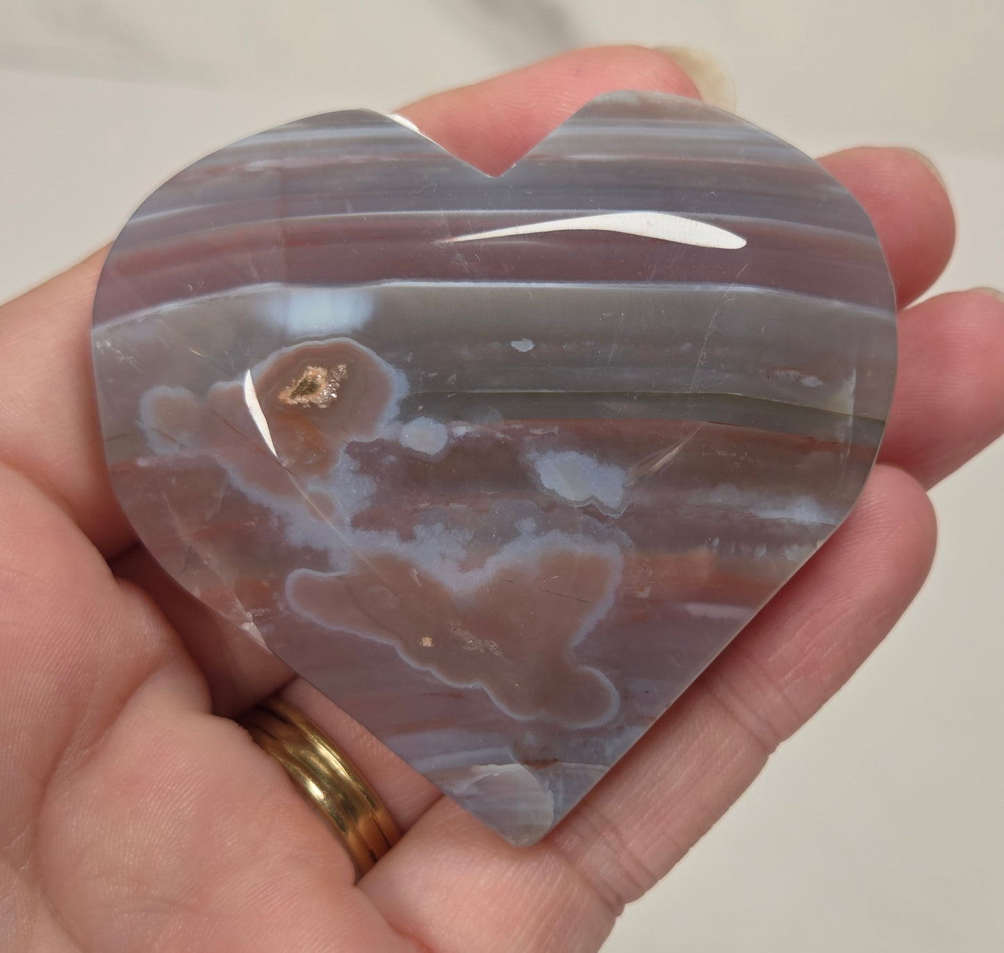 A heart-shaped polished agate stone with natural banding in gray, white, and brown, held in a person's hand.