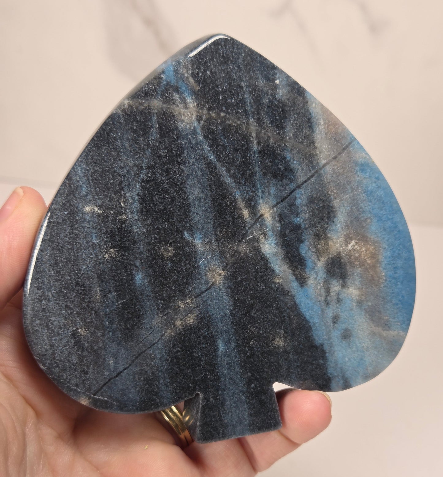 A hand holding a teardrop-shaped black and blue speckled stone object, likely a decorative piece or compact mirror, against a light marble-patterned background.