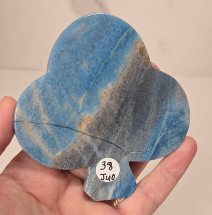 A hand holding a teardrop-shaped blue stone carving with natural marbling and a small white sticker reading '38 J40' on the bottom edge.
