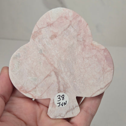 A hand holding a small, teardrop-shaped pink marble piece with natural veining and a small handwritten paper tag that reads '38 JWN'.