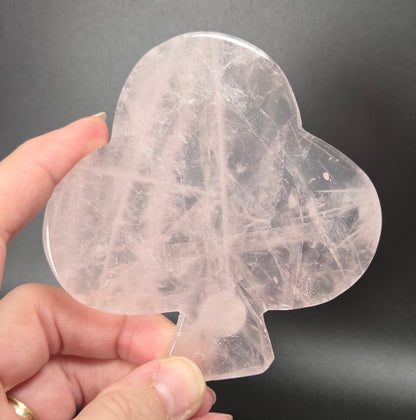 A hand holding a transparent, club-shaped crystal or stone piece against a dark gray background.