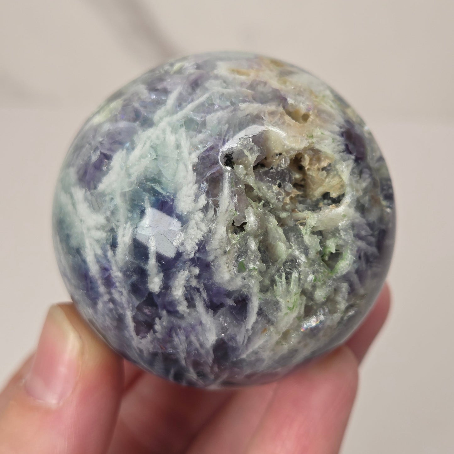 A hand holding a polished round stone with marbled blue, white, and gray veining and a rough textured area near the top right.