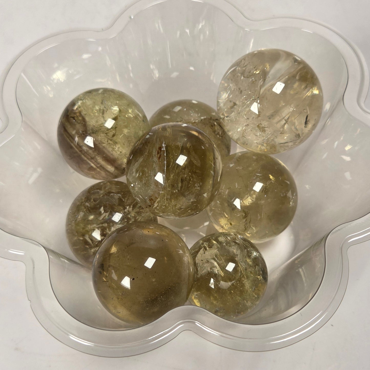 Several round, translucent smoky amber or honey-colored glass marbles resting in a small clear plastic flower-shaped dish on a plain white surface.