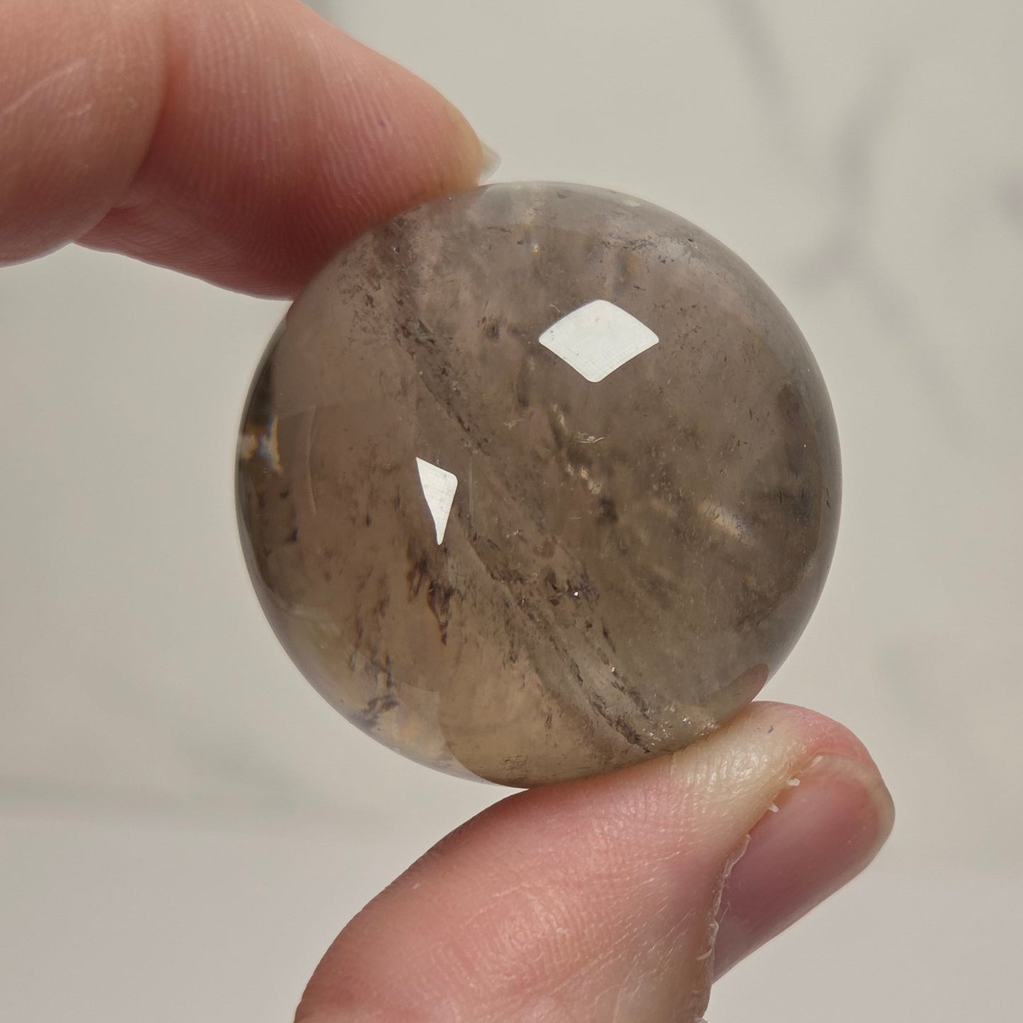 A hand holding a polished round stone bead with natural brown and gray marbling, set against a light gray marble-patterned background.