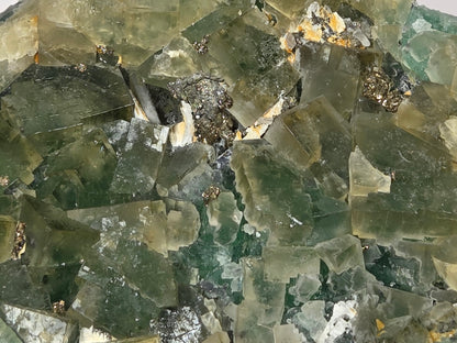A close-up of a translucent green crystal cluster with layered, geometric facets and natural mineral inclusions.
