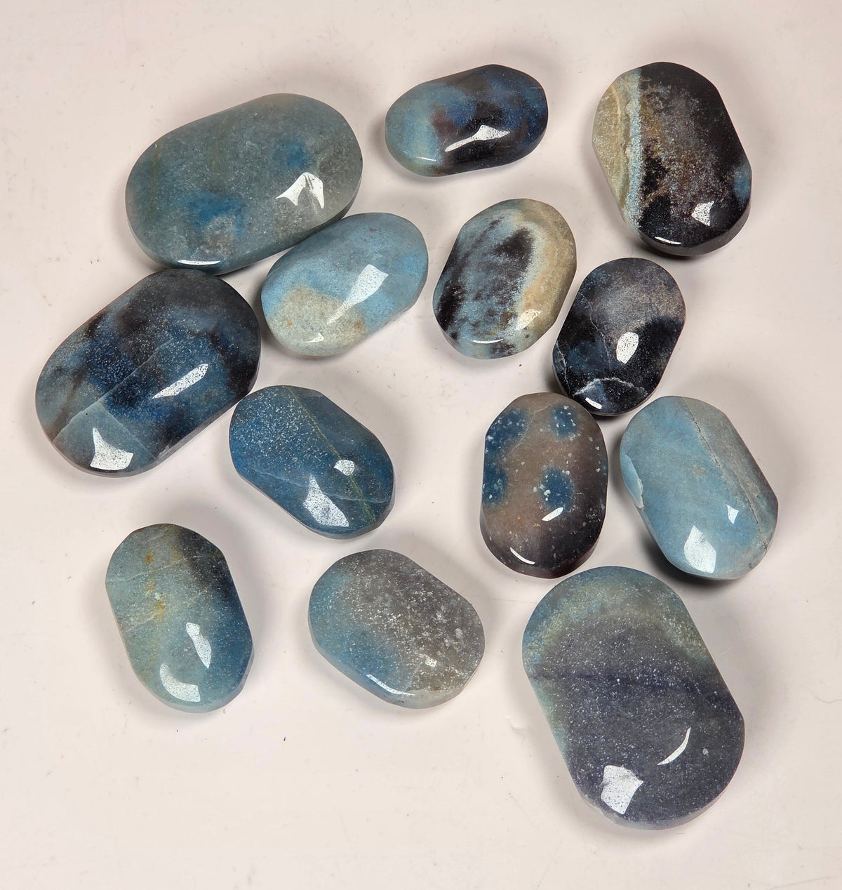 A set of polished blue tumbled stones in various shapes and sizes, arranged on a plain off-white background.