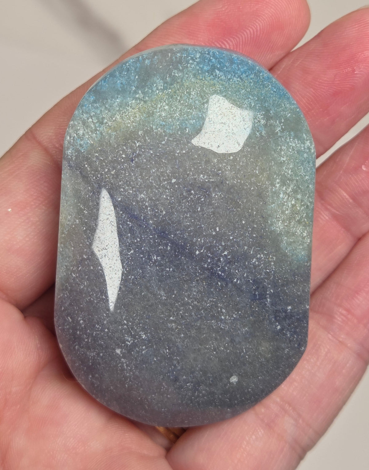 A hand holding a polished, rounded rectangular gemstone with a blue, gray, and white speckled cosmic or starry pattern.