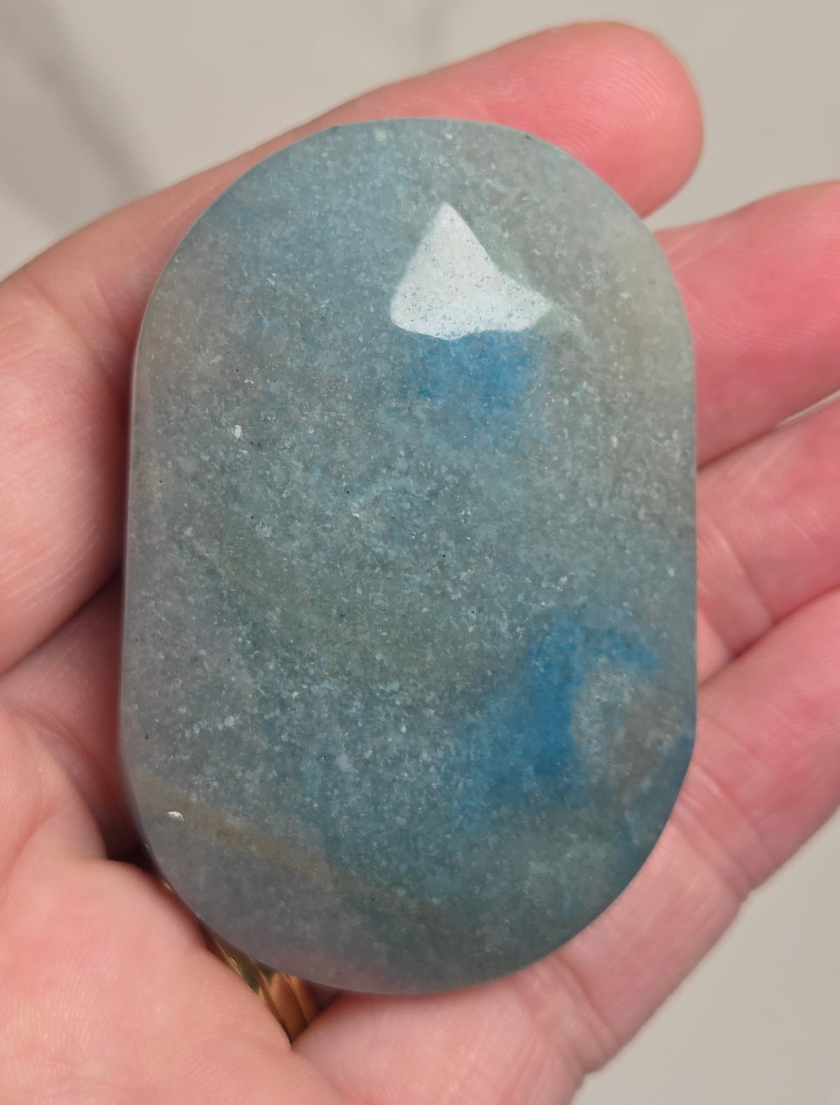 A hand holding a polished, rounded blue stone with natural marbled patterns of teal, blue, and gray.
