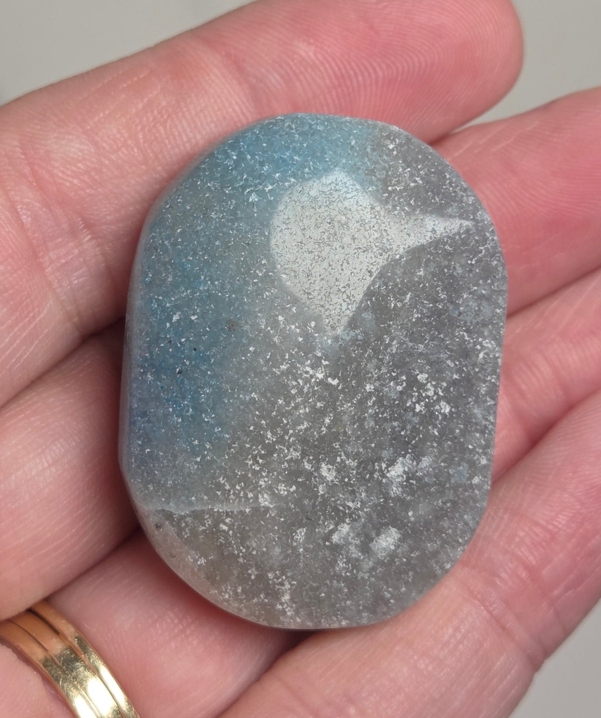A polished tumbled stone with a blue-gray and white marbled pattern, held in a person's hand.
