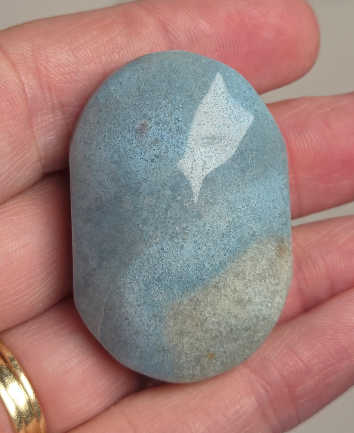 A polished, smooth oval-shaped stone with a light blue and white marbled pattern, held in a person's hand.