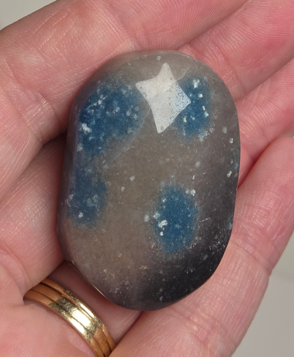A polished tumbled stone with a gray base and blue cloudy patterns, held in a person's hand.