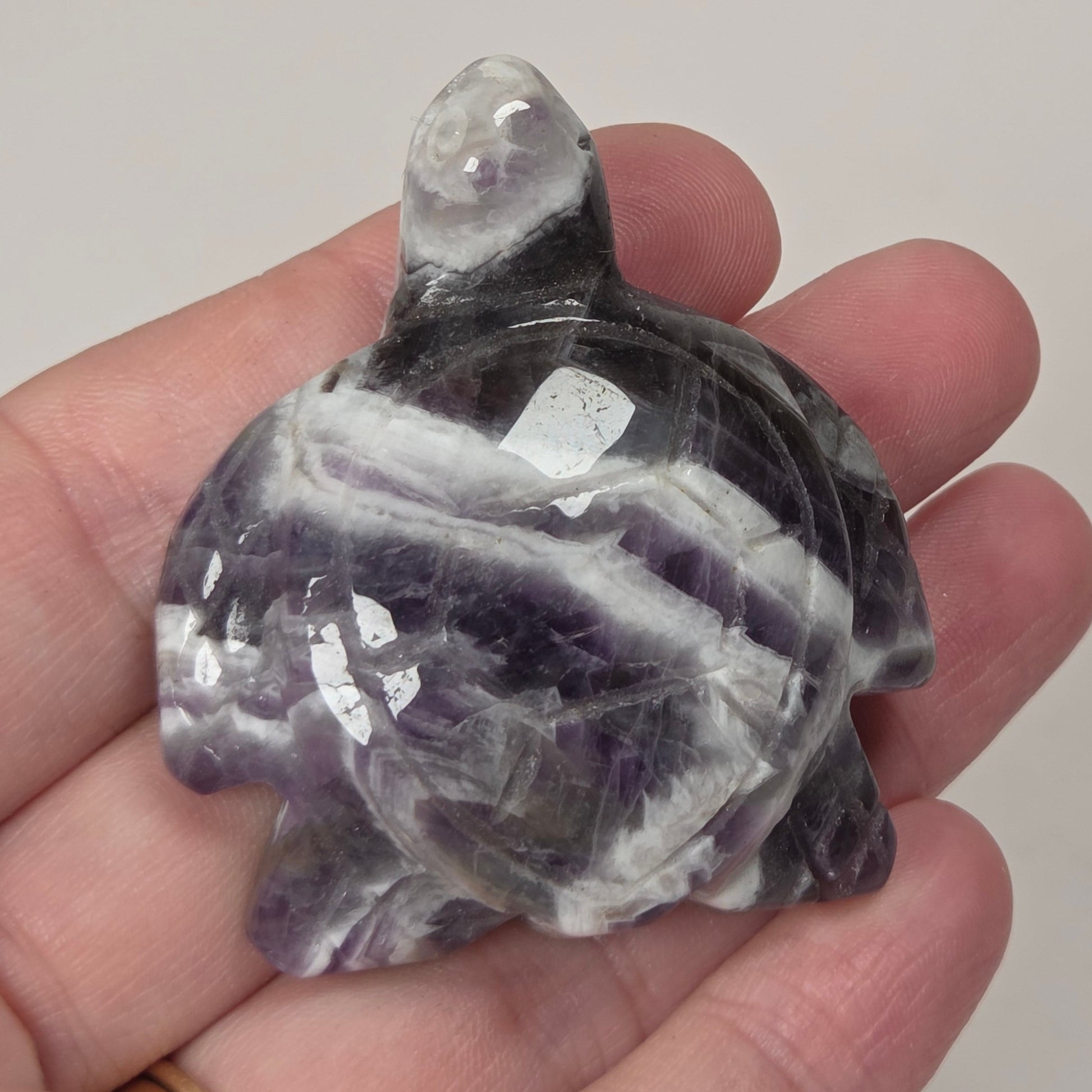 A hand holding a polished carved stone turtle, likely amethyst, showing natural purple and white banding.