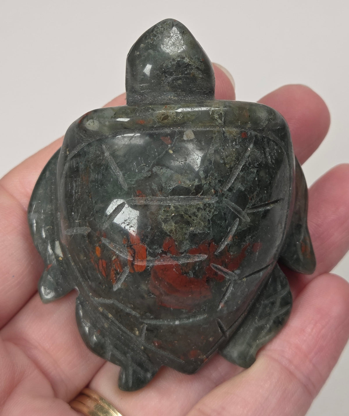 A carved turtle figurine made of dark green stone with red matrix inclusions, held in a person's hand against a plain light background.