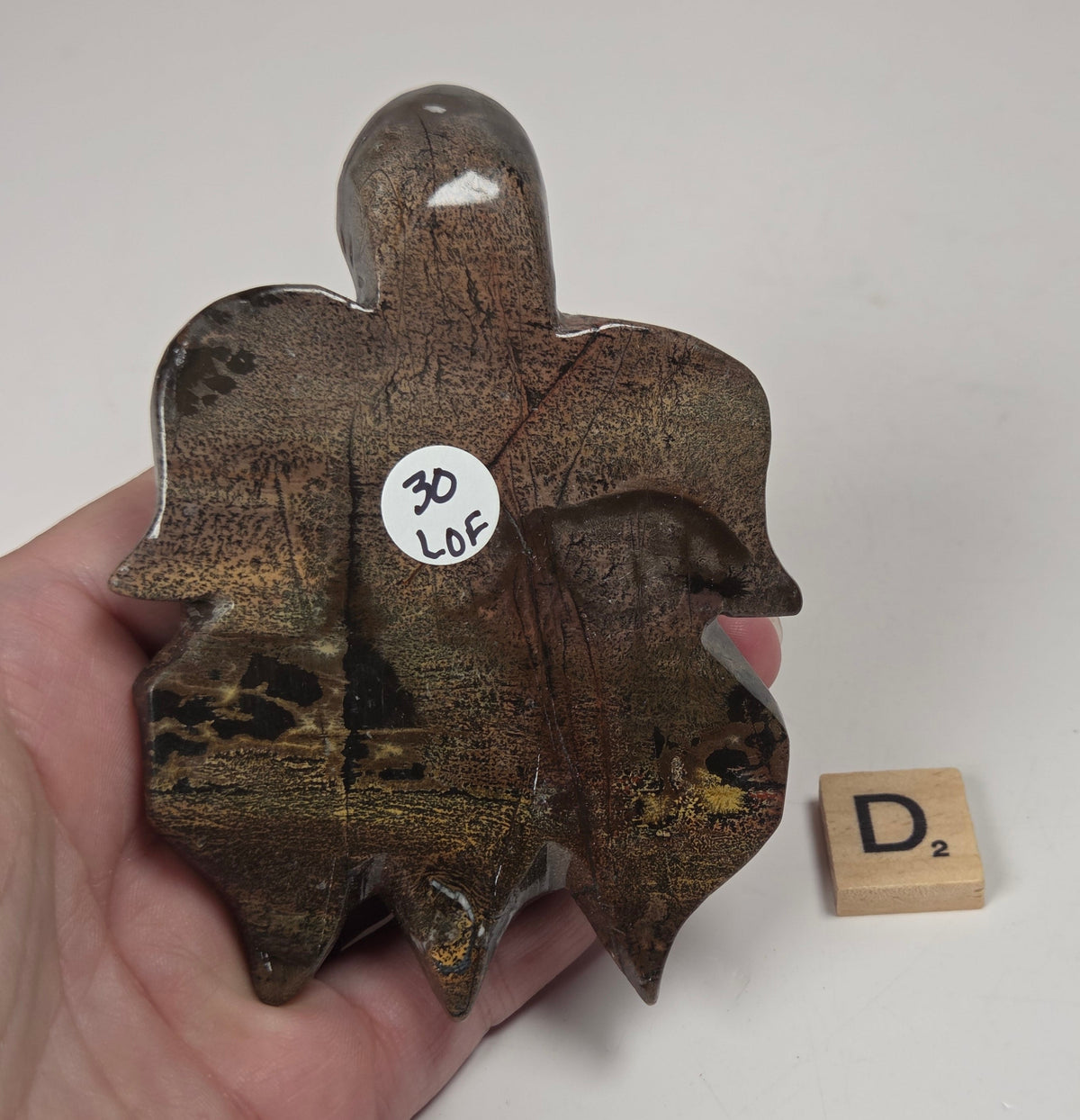 A hand holds a small, irregularly shaped polished stone or crystal specimen with a rough, earthy brown and gold crystalline texture. A small white sticker on the object reads '30 Lof'.