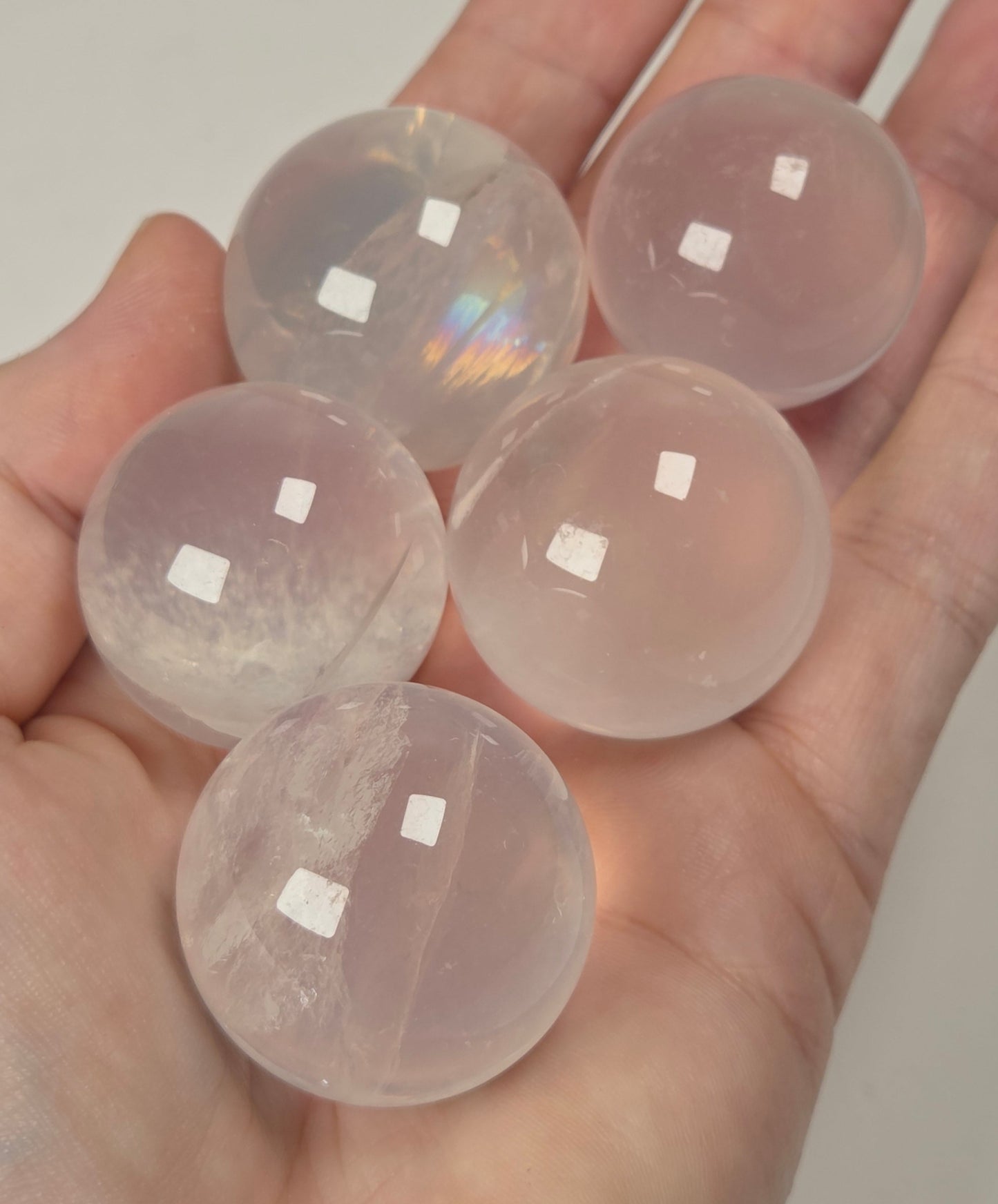 Five smooth, translucent pale pink crystal spheres resting in an open hand against a plain light background.
