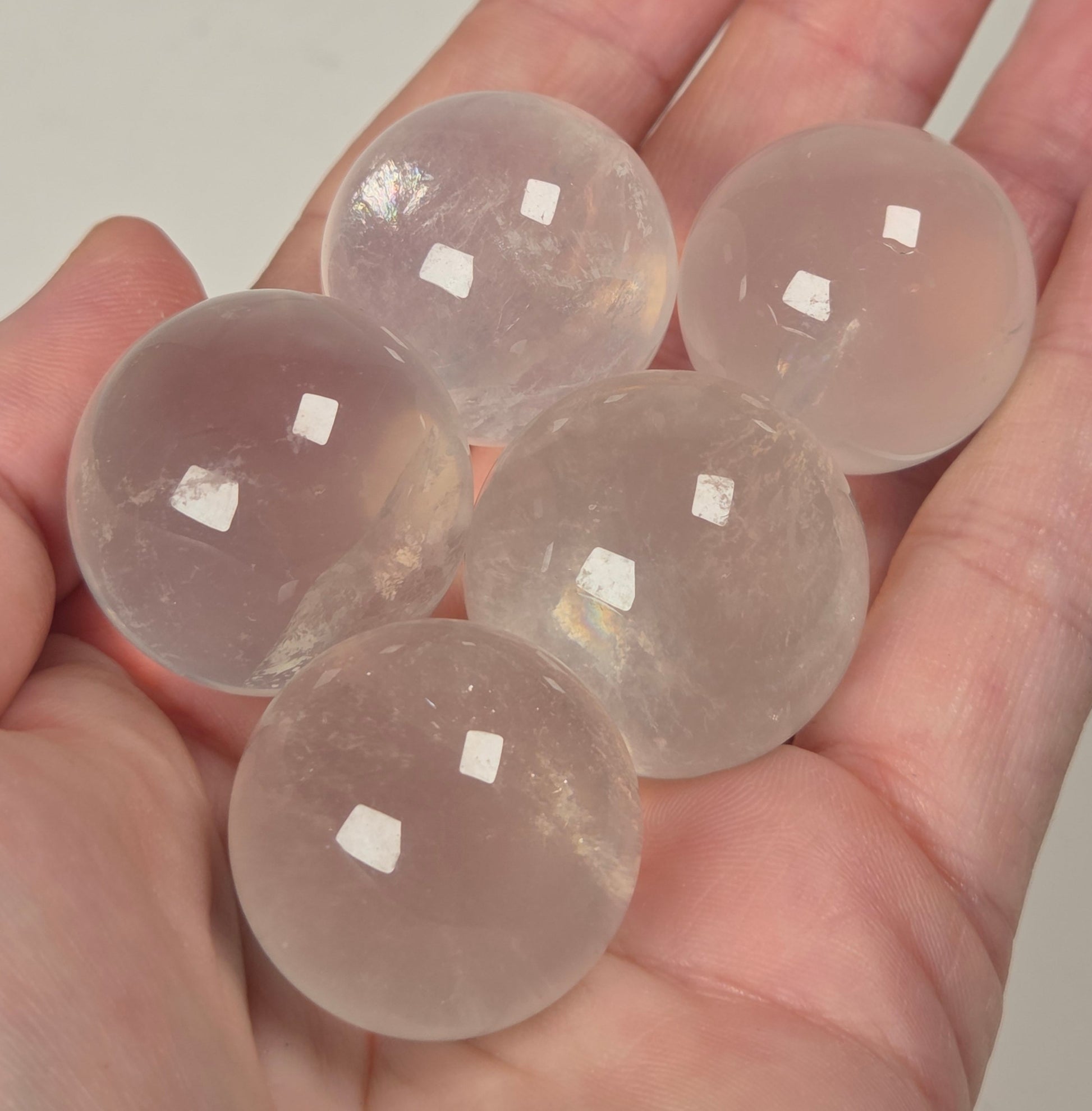 Five smooth, polished translucent pale pink spheres resting in an open hand against a plain light background.