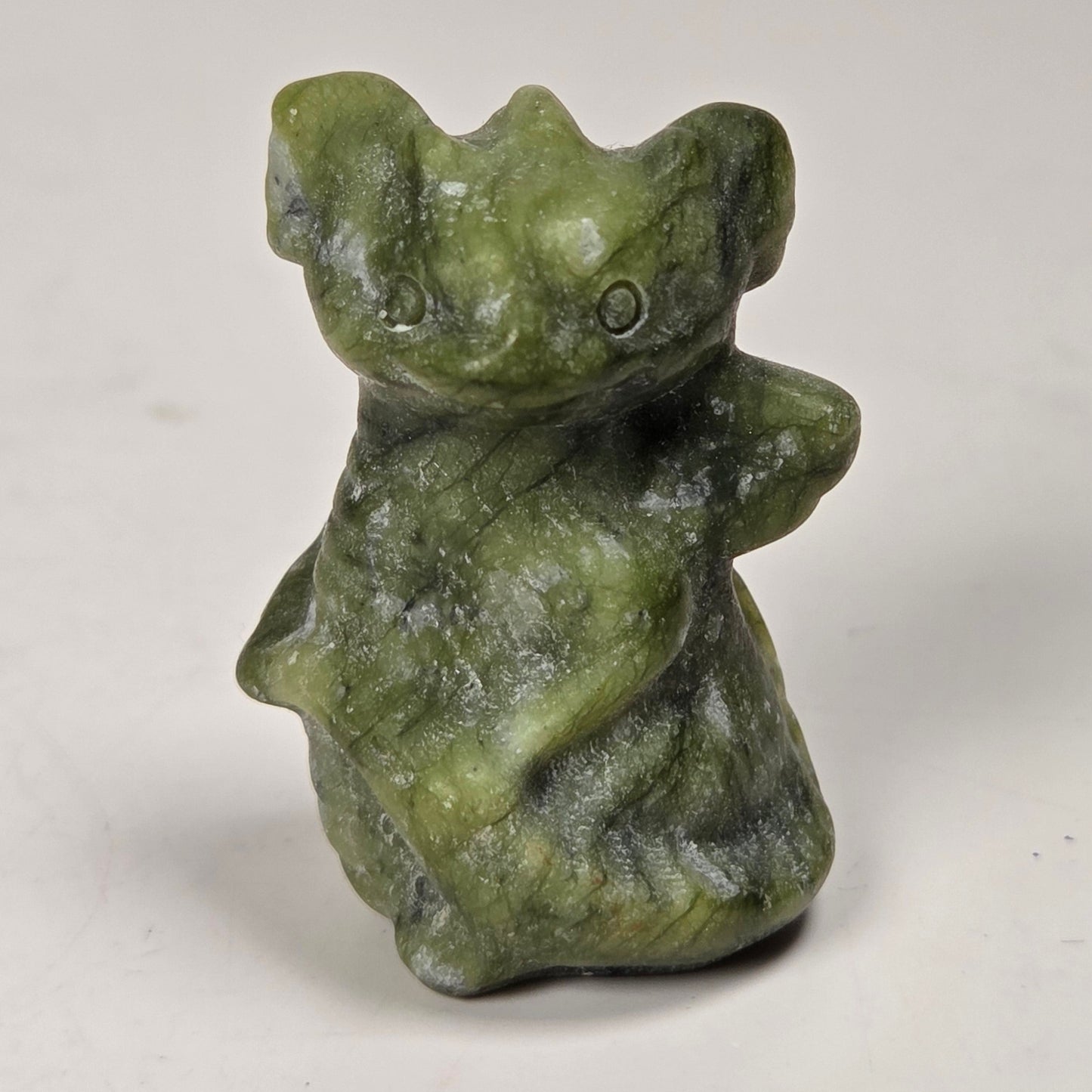 A small carved figurine of a crouching animal, likely a bear or wolf, made from green stone with natural marbling, set against a plain light gray background.