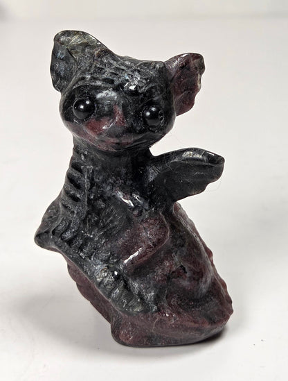 A small dark figurine of a dragon with large ears and glossy black eyes, standing on a plain light background.