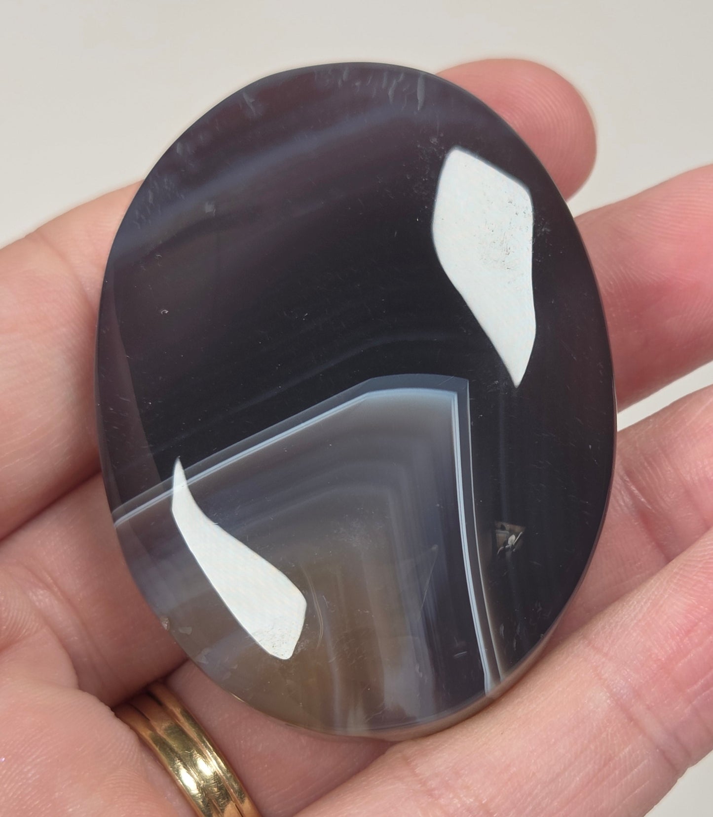 dark banded agate palm carving being held in a hand against a white background