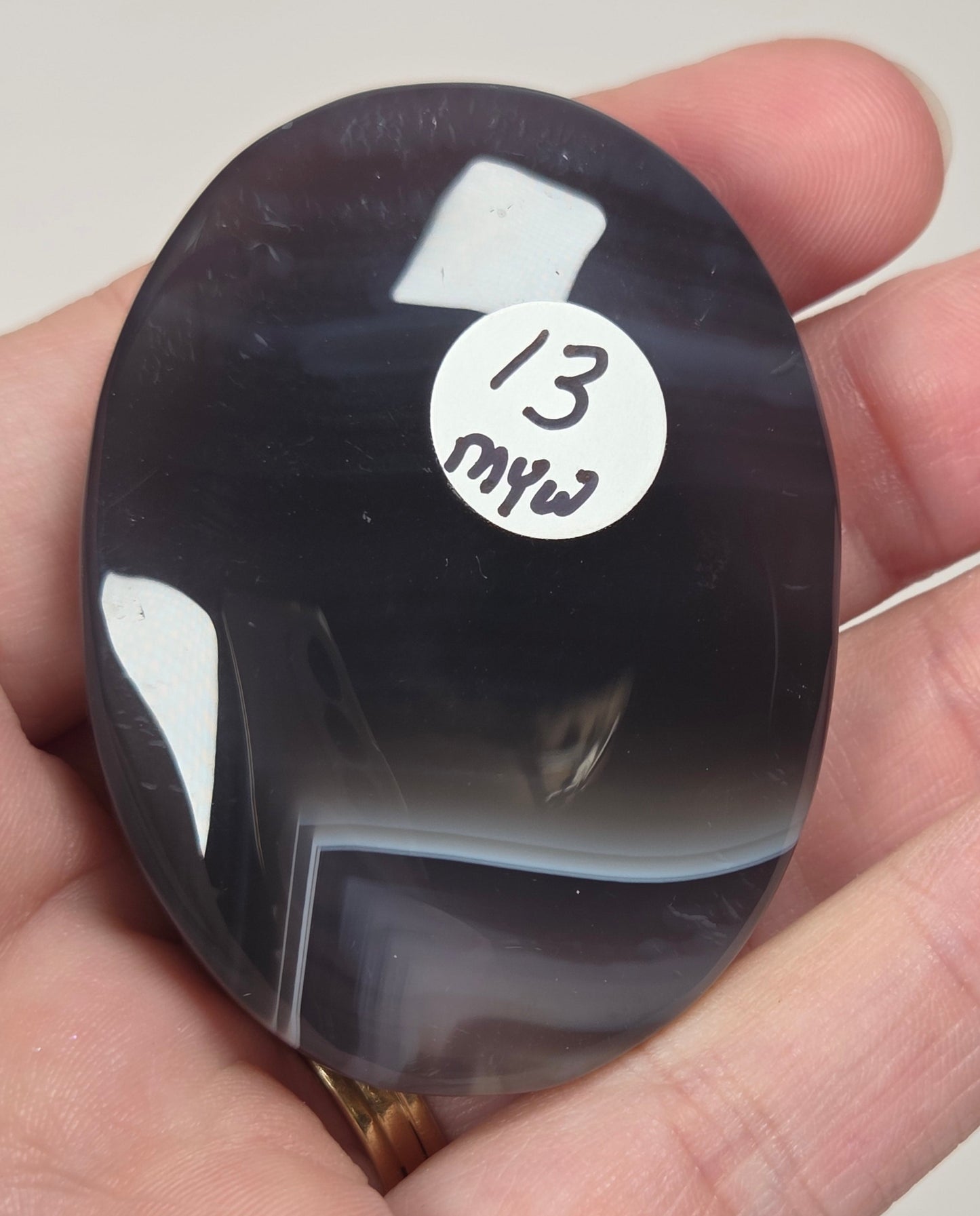 dark banded agate palm carving being held in a hand against a white background