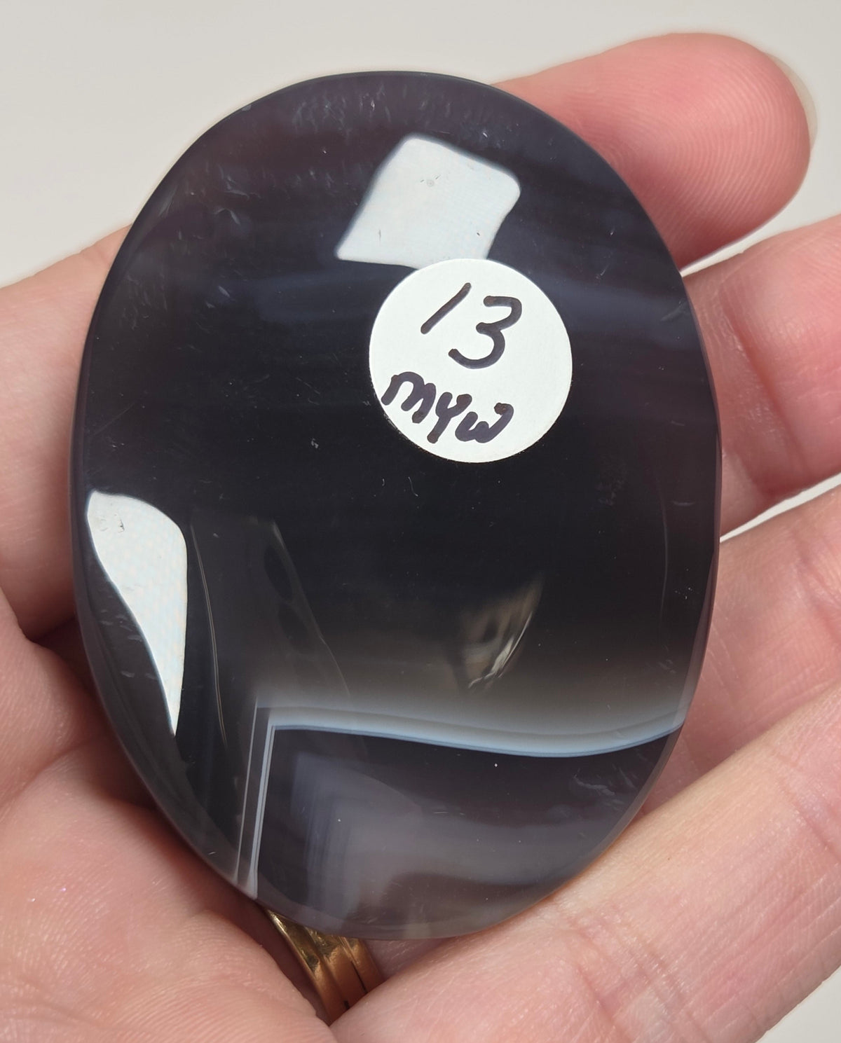 dark banded agate palm carving being held in a hand against a white background