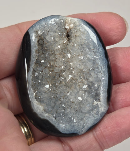 Black agate palm carving with white quartz crystals being held in a hand against a white background