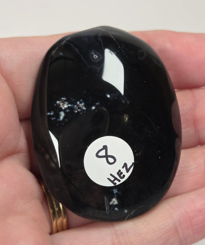 Black agate palm carving  being held in a hand against a white background