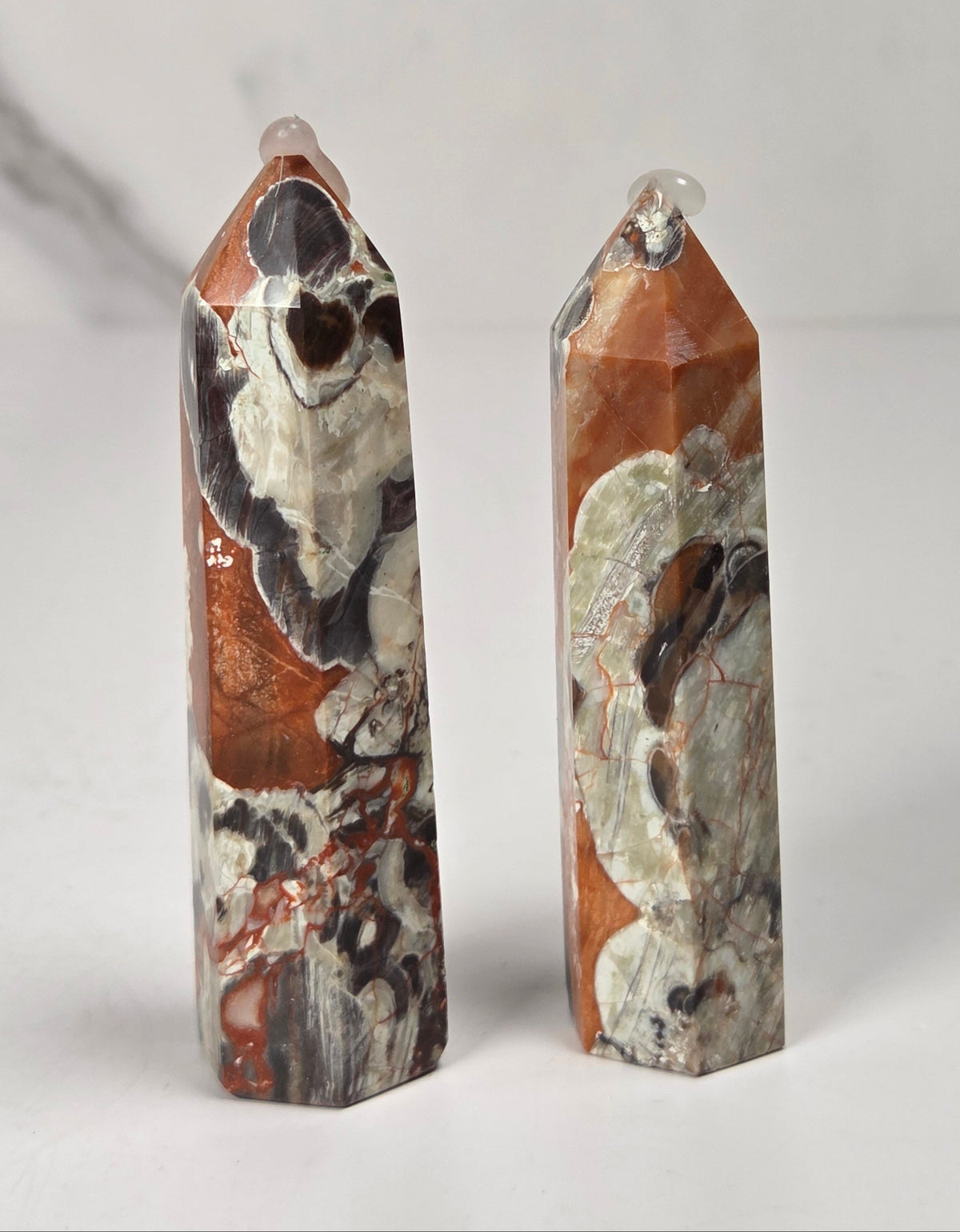 A tall, narrow decorative crystal tower made of natural copper pyrite and silver quartz with brown and orange mineral inclusions, standing upright on a white surface against a light gray marble-patterned background.