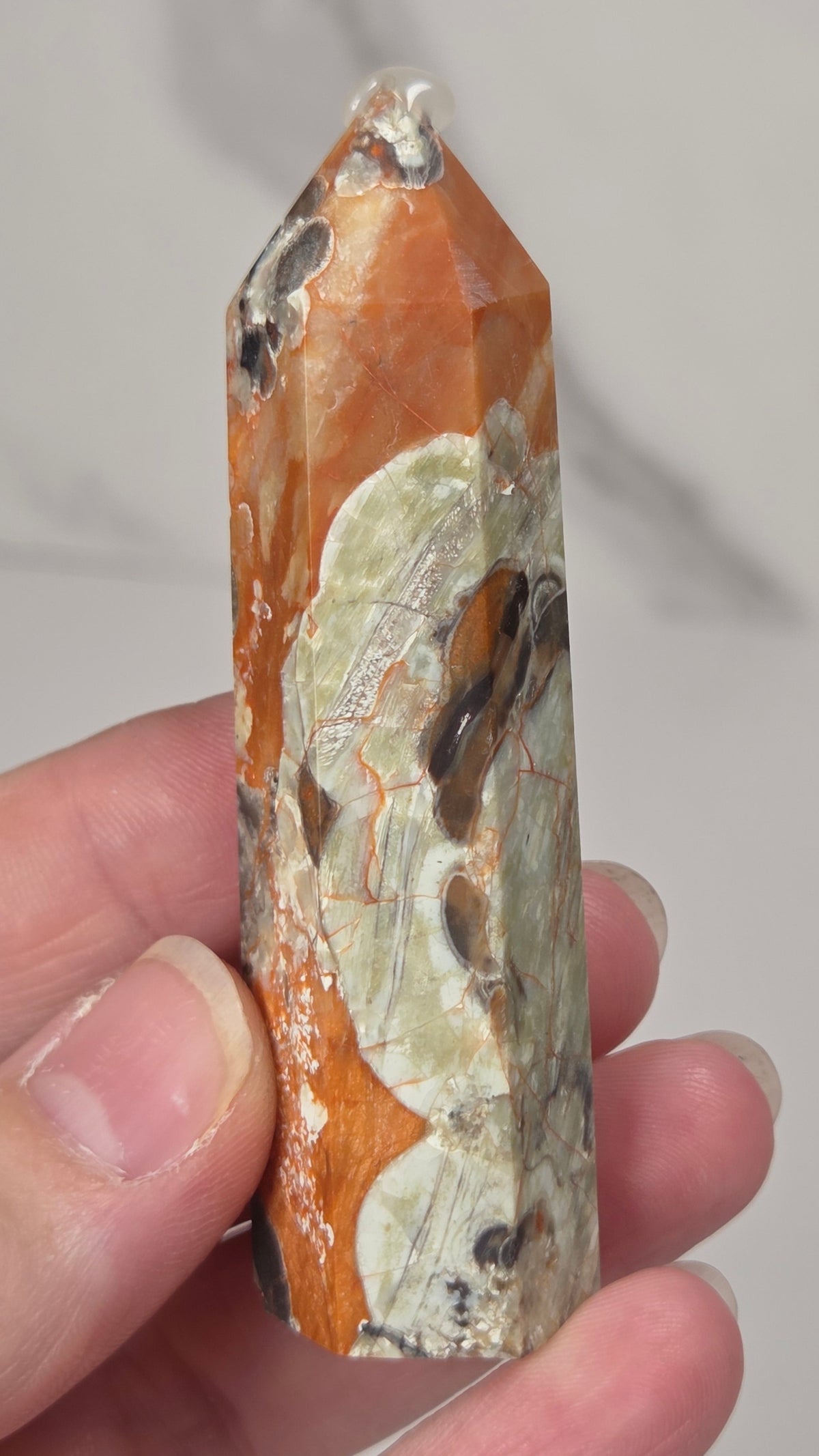 A hand holding a natural pointed crystal tower showing orange, beige, and gray patterns.