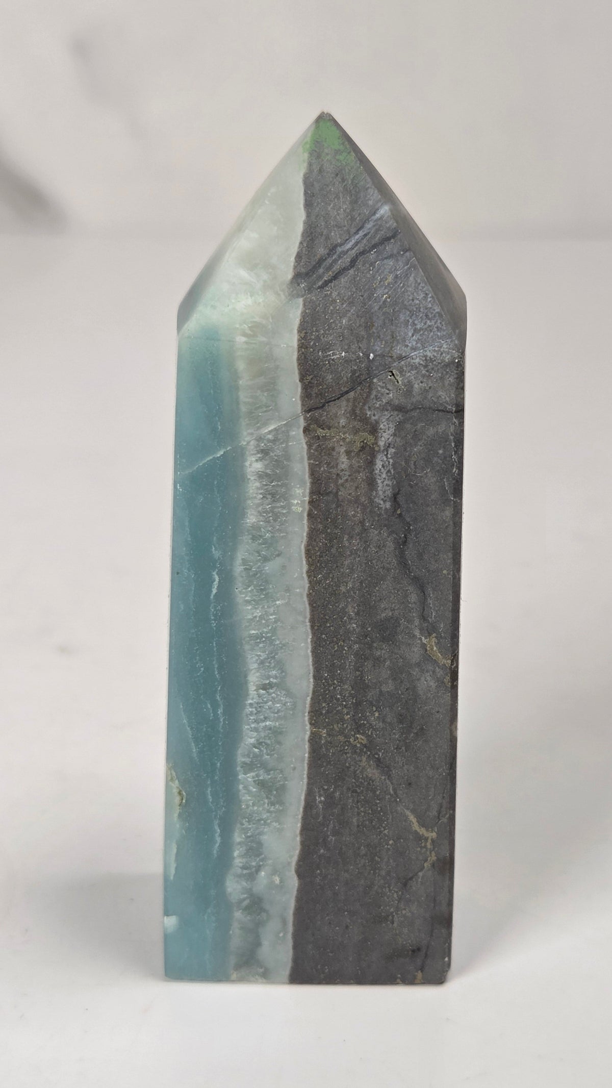 A polished mineral crystal tower with a split dual-color design, featuring light blue and white on one side and dark gray with subtle gold veining on the other, set against a neutral light gray background.