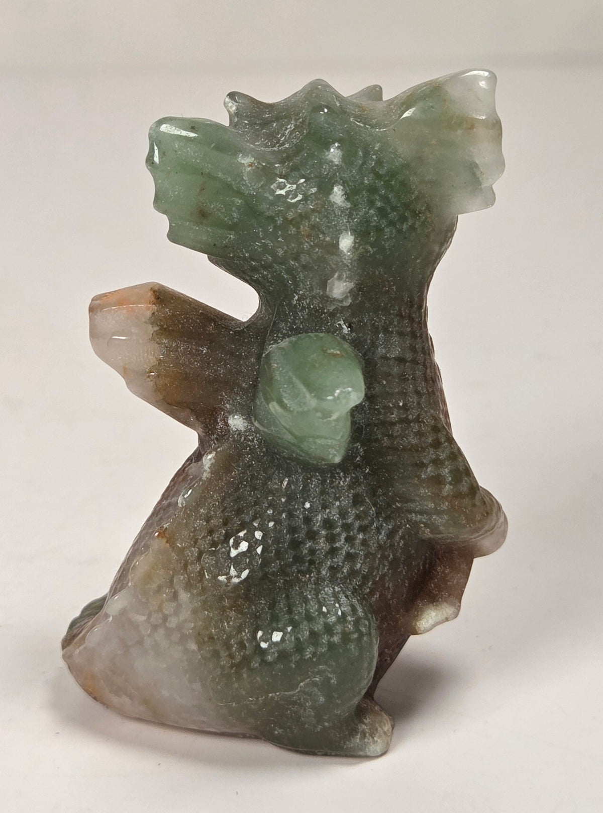 A small carved figurine of a dragon made from green and brown marbled stone, standing on a plain light background.