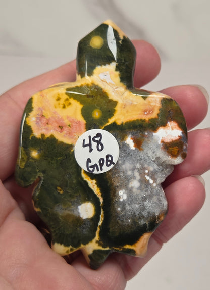 A hand holding a polished carved stone turtle figurine with marbled green, orange, pink, and cream patterns.