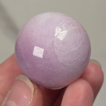 Hand holding a purple and white crystal sphere against a neutral background