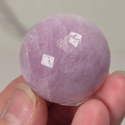 Hand holding a purple and white crystal sphere against a neutral background