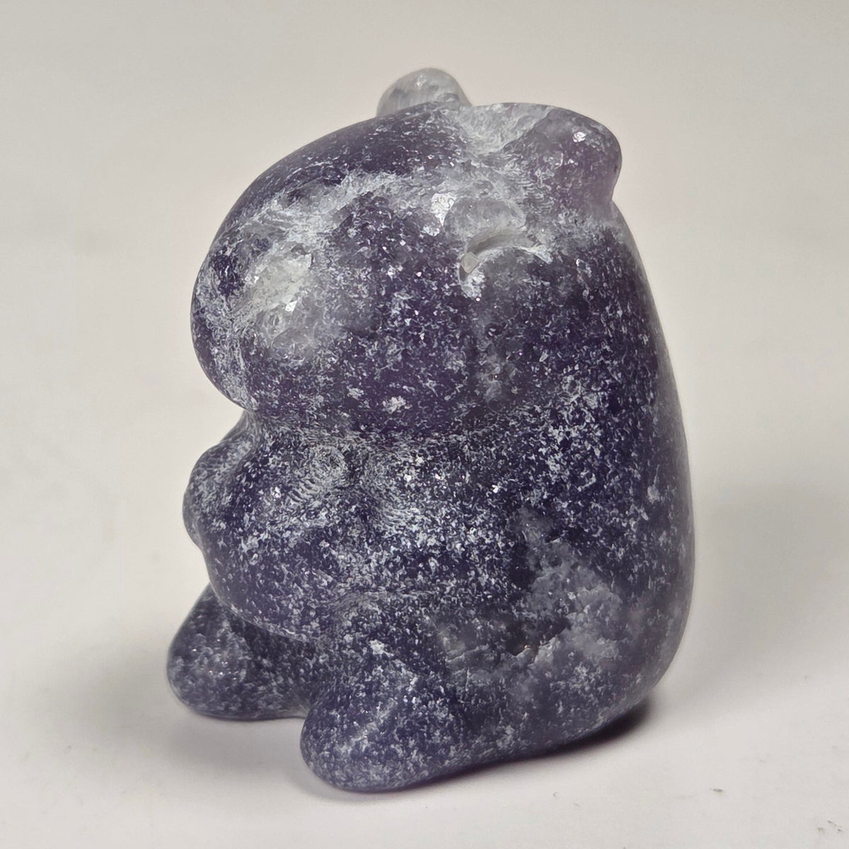 A small carved stone figurine of a rabbit, made from a speckled purple and white stone, standing on a light gray surface.